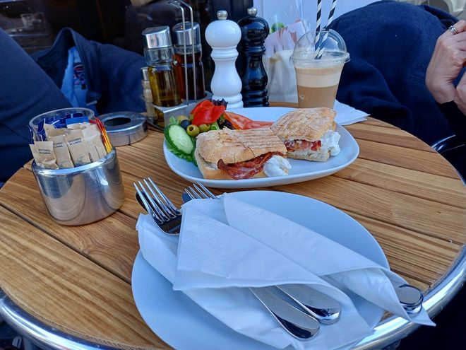 A wide view of a terrace table laid with lunch and an iced coffee