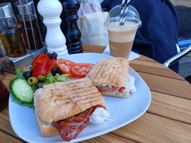 A bacon and tomato panini with salad and an iced latte outside